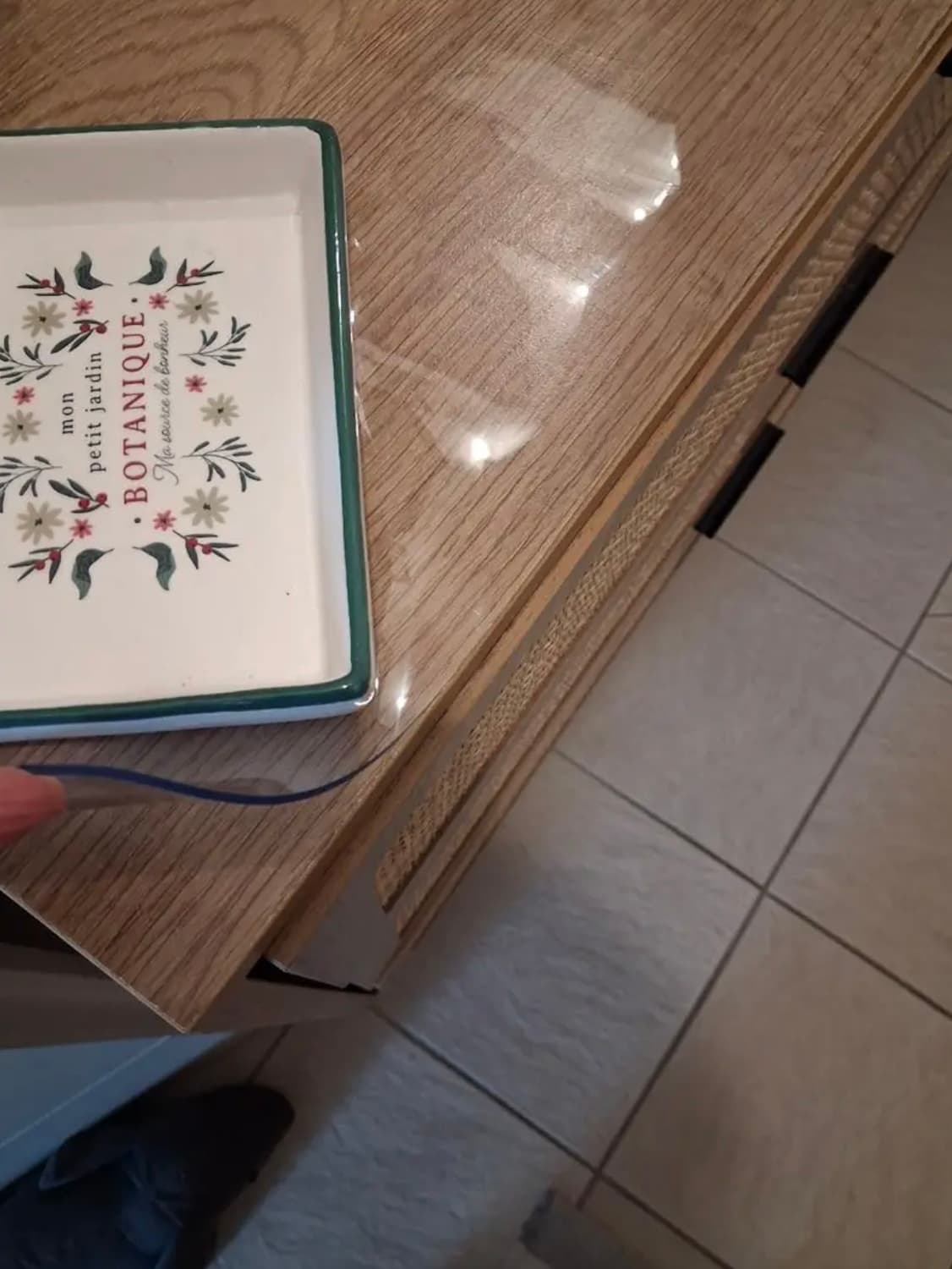 Róg dębowej komody z ozdobną tacą; dłoń przytrzymuje krawędź przezroczystej nakładki